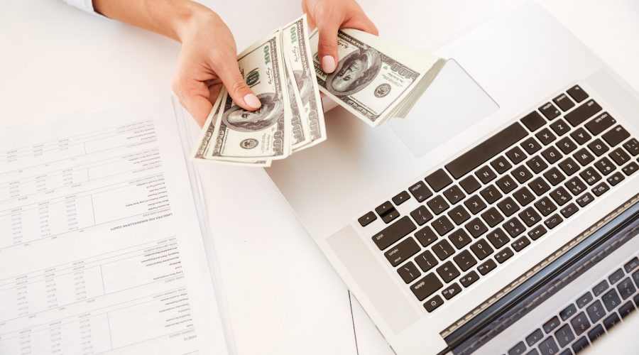 Cropped image of businesswoman sitting in her office and holding money near laptop