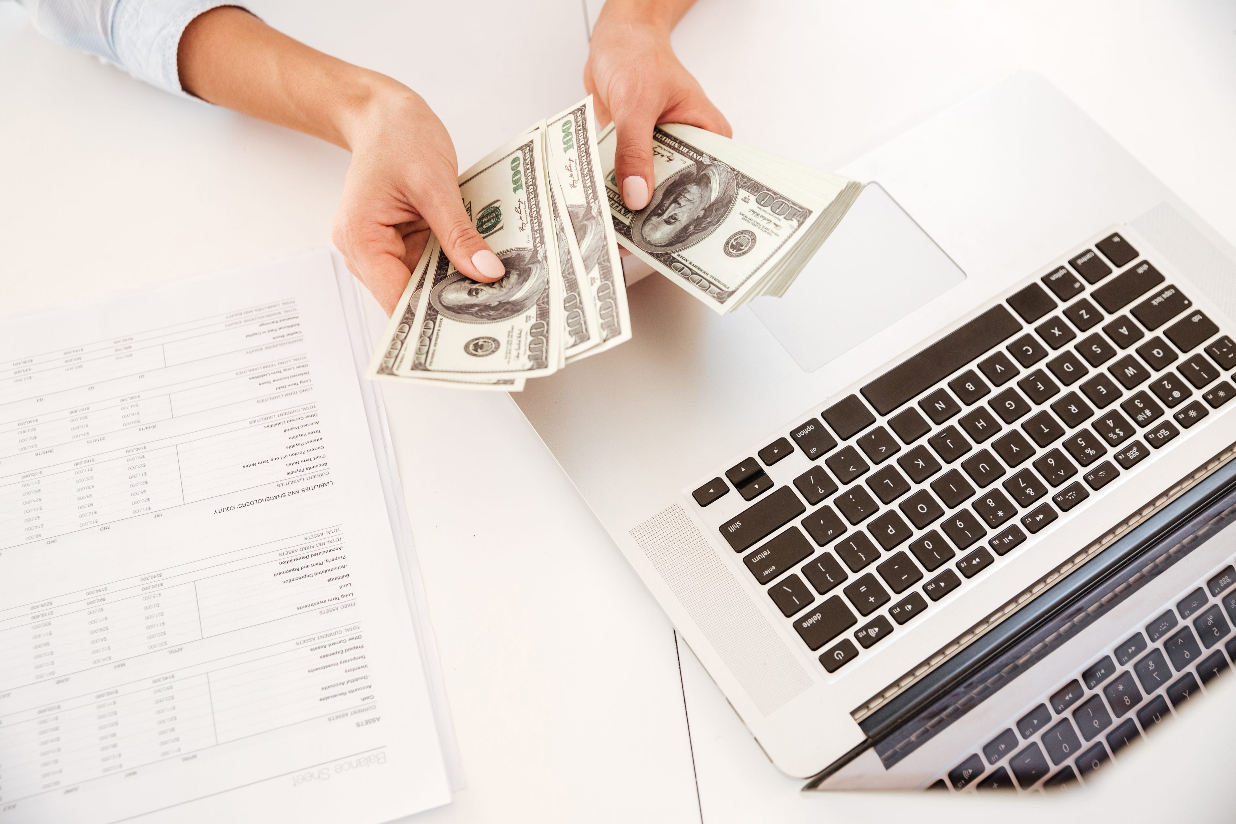 Cropped image of businesswoman sitting in her office and holding money near laptop