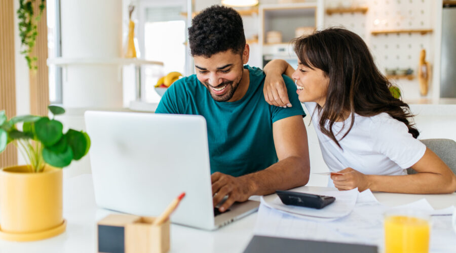 A young responsible African American couple sits at home and calculating monthly income. The man is looking at the laptop while the woman explaining to him how to save some money.